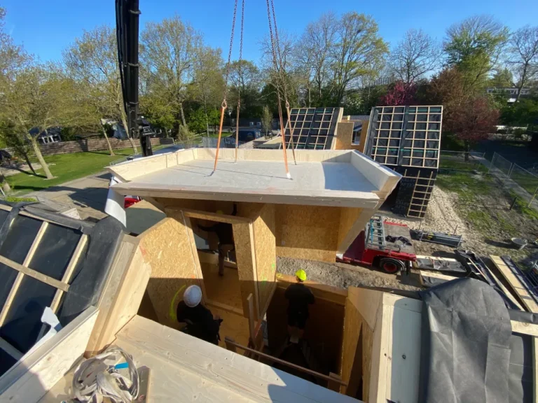 Kraan hijst een prefab element op zijn plek tijdens de montage van een houtskeletbouwwoning